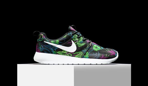 Nike sneaker with floral pattern on a white platform against a black background.