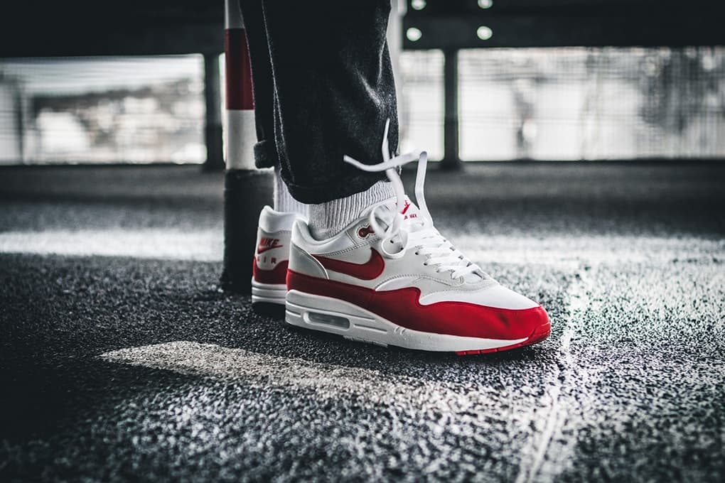 Nike Air Max 1 sneakers in red and white on asphalt, worn by a person in dark pants.