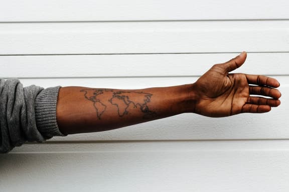 Forearm with minimalist world map tattoo against white background.