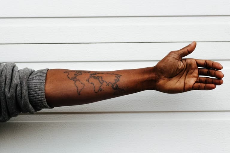 Forearm with minimalist world map tattoo against white background.