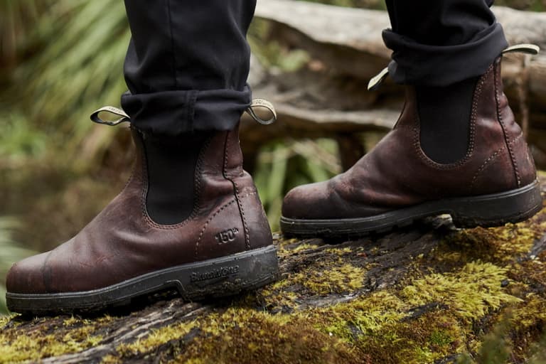Blundstone 150th Anniversary boots in brown leather on mossy log outdoors.