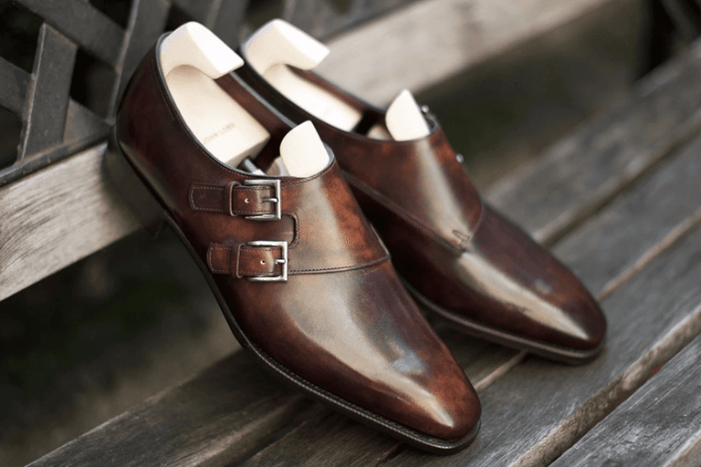 John Lobb brown leather double monk strap shoes on a wooden bench.