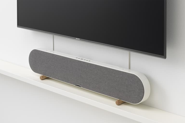 Yamaha soundbar in grey fabric finish on a white shelf beneath a wall-mounted TV.