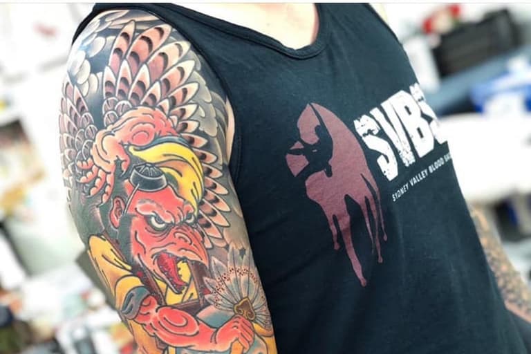 Person with colourful sleeve tattoo wearing a black tank top featuring a logo.