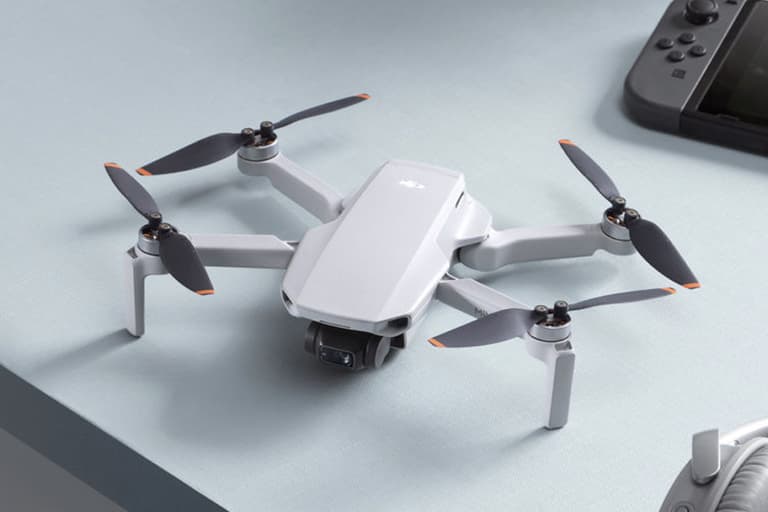 DJI Mini 2 drone on a light blue table with gaming console nearby, showcasing its compact design and grey finish.