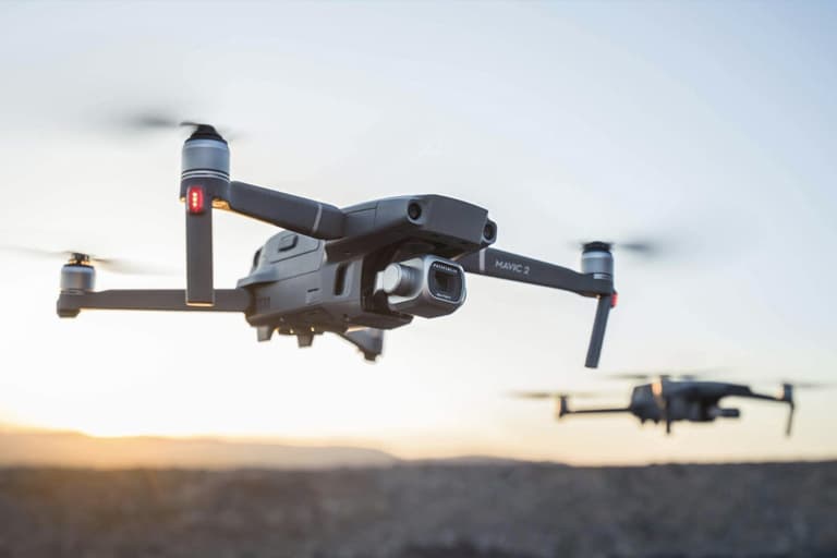 DJI Mavic Pro 2 drone flying at sunset with Hasselblad camera, another drone in the background.