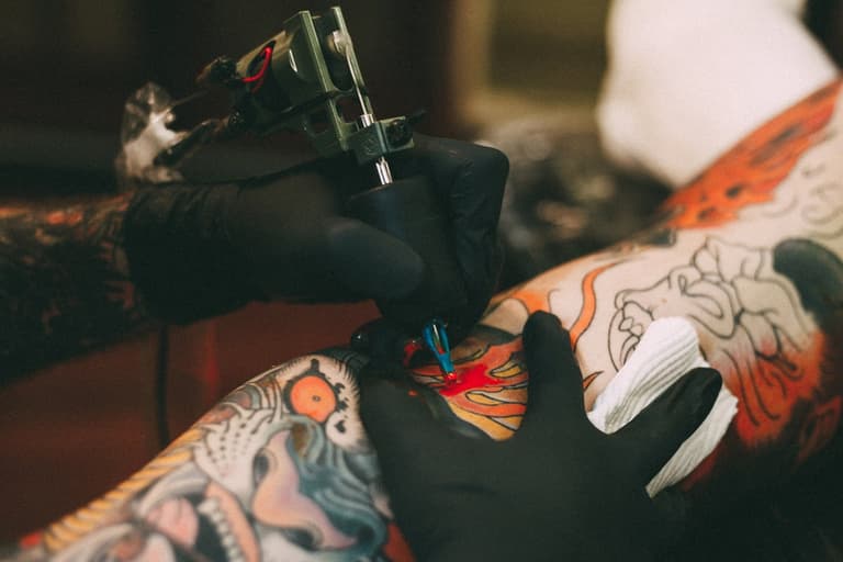 Tattoo artist with black gloves inking colourful design on a client's arm in a Brisbane studio.