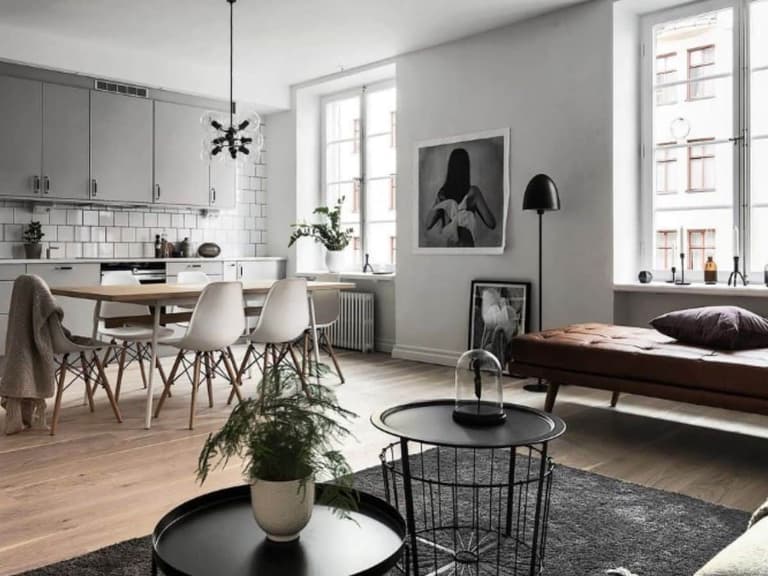 Scandinavian-style living room with minimalist decor, featuring grey cabinets, white chairs, and a brown leather sofa.