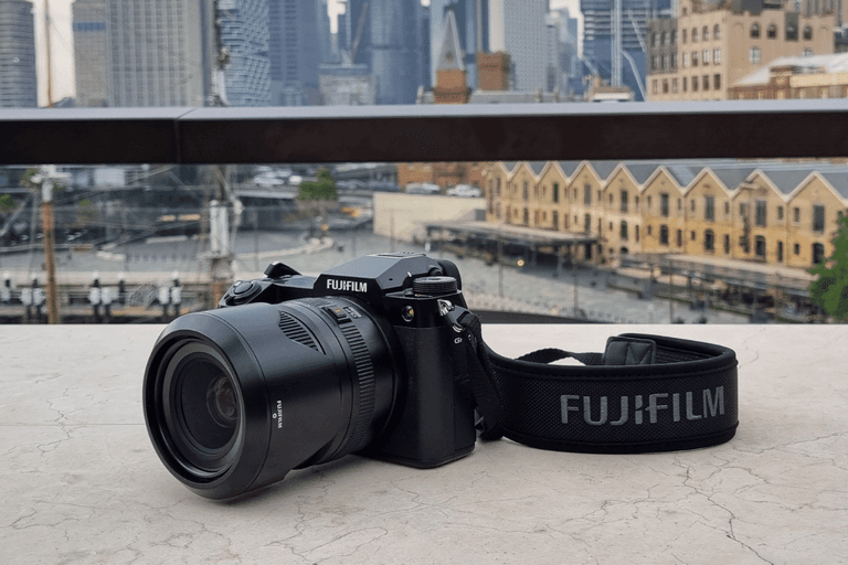Fujifilm GFX100S camera with lens on marble surface, city skyline in background.