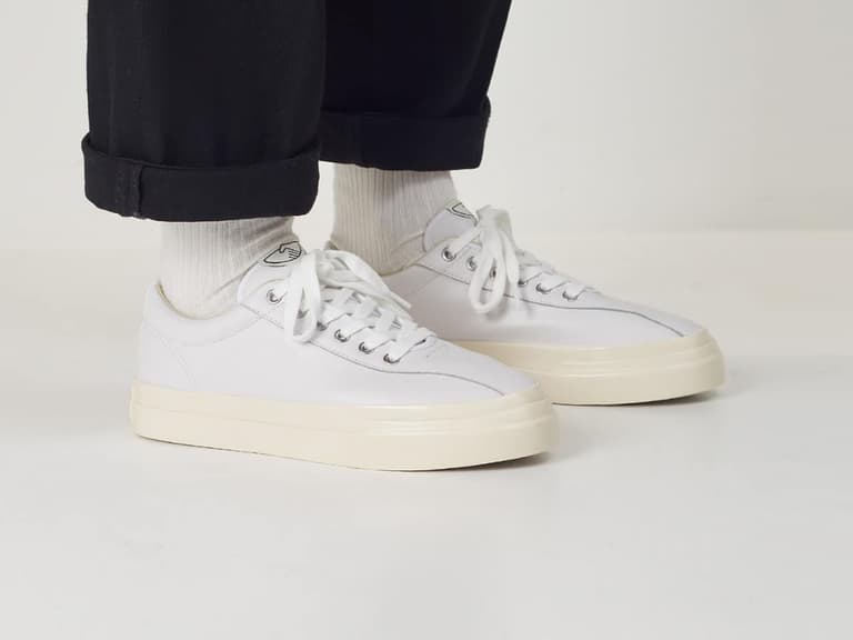 White sneakers with cream soles worn by person in black pants and white socks.