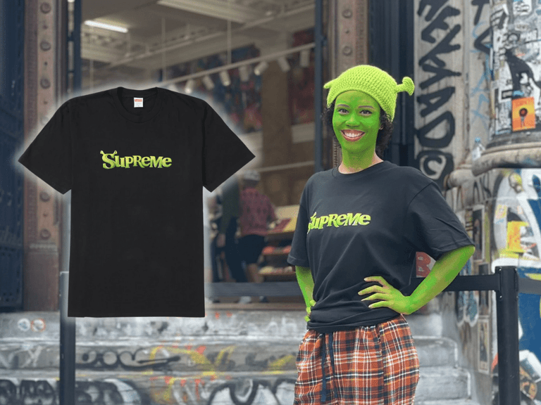 Person wearing Supreme Shrek T-shirt and green face paint stands outside graffiti-covered building.