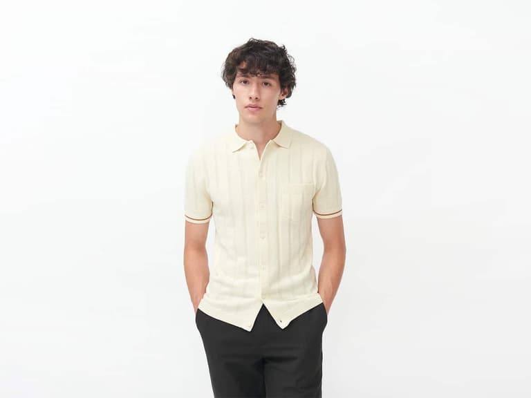 Man wearing Percival Purl Weave Cuban knit shirt in cream with black trousers against a white background.