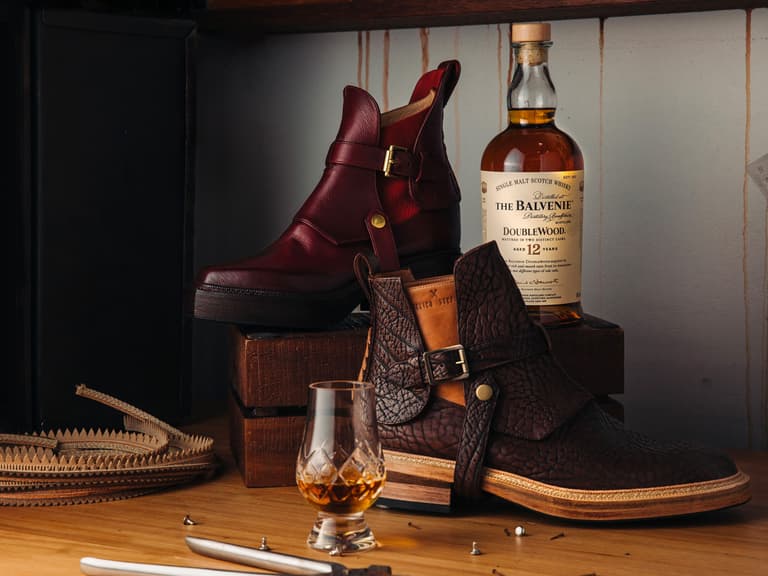 Atelier Stefani bespoke boots in rich leather displayed with The Balvenie DoubleWood 12 Year Old whisky bottle on a wooden surface.