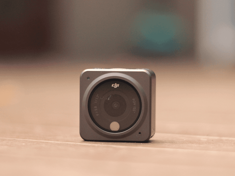 DJI Action 2 camera in grey, front view, resting on a wooden surface with blurred background.