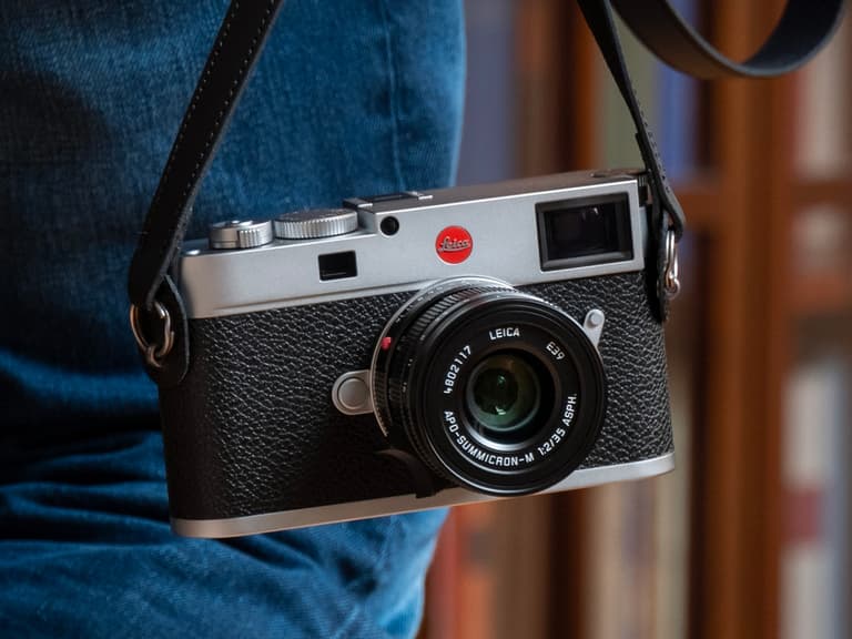 Leica M11 camera with black leather grip hanging from a strap, featuring a 60MP lens.