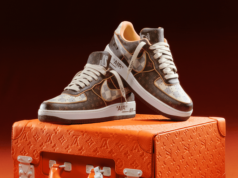 Louis Vuitton x Nike Air Force 1 sneakers with monogram pattern on orange textured suitcase.