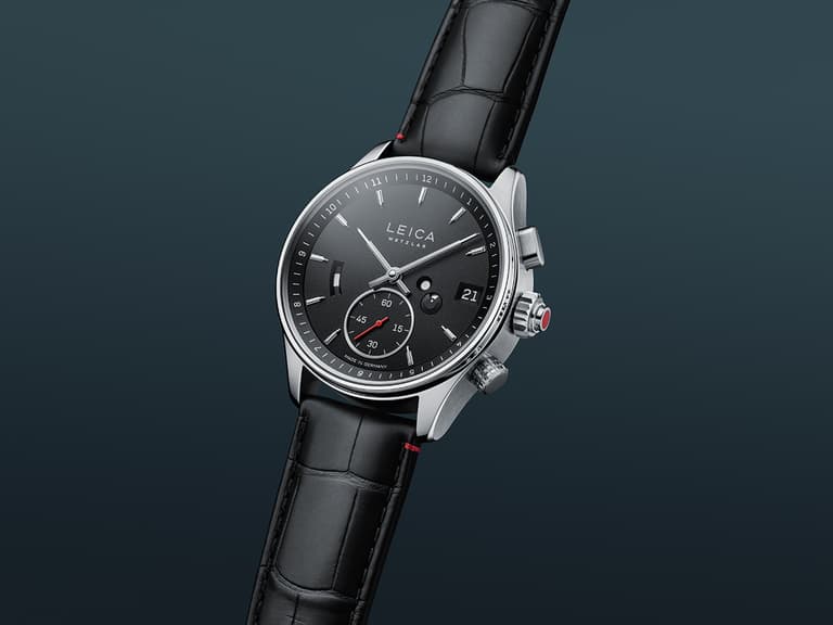 Leica L1 watch with black dial and leather strap on a dark gradient background.