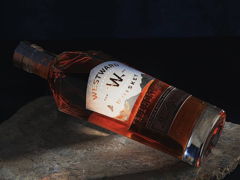 Westward American Single Malt Whiskey bottle on a dark stone surface, illuminated dramatically.