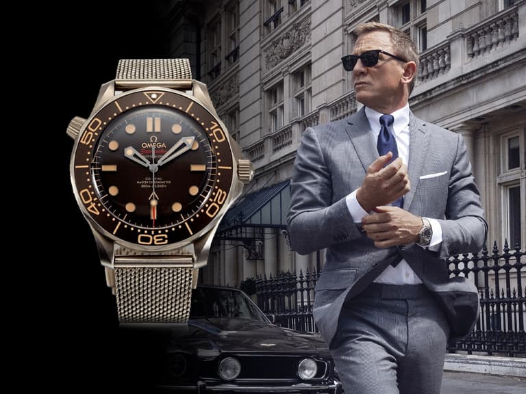 Omega Seamaster watch with brown dial and mesh bracelet, worn by a man in a grey suit and sunglasses, standing near a classic car.