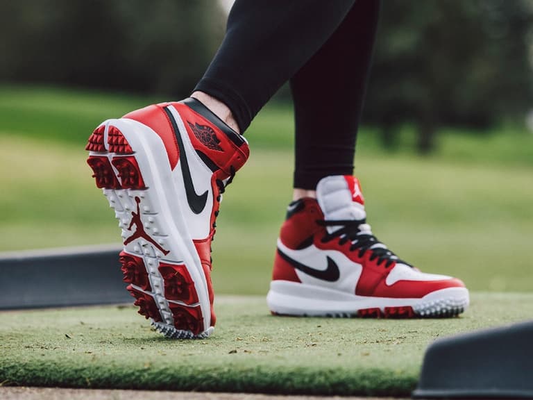 Nike Air Jordan golf shoes in red, white, and black on a grassy golf course, highlighting the sole design.