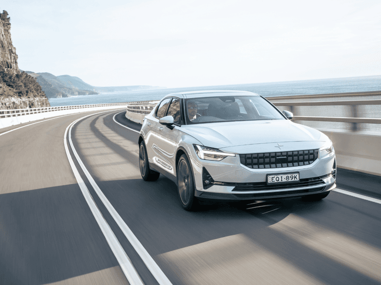 Polestar 2 in white driving along the scenic Great Ocean Road with ocean views and cliffs in the background.