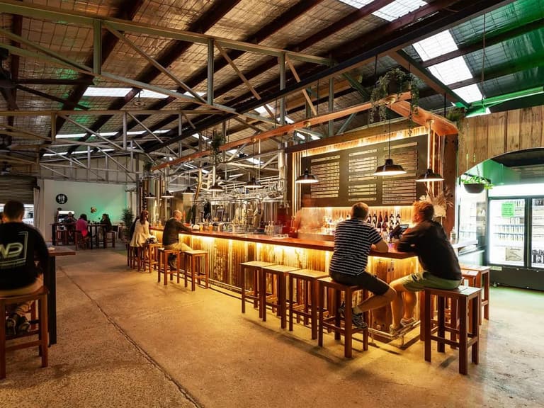 Bucketty's Brewing Co interior with patrons seated at a rustic wooden bar under warm lighting.