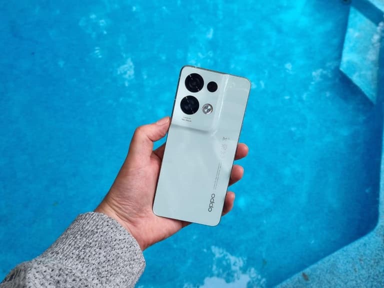 Oppo Reno8 Pro in hand against a bright blue pool background, showcasing its sleek design and triple camera setup.