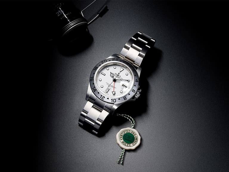 Rolex Explorer II watch with white dial and stainless steel bracelet on black surface, green tag nearby.