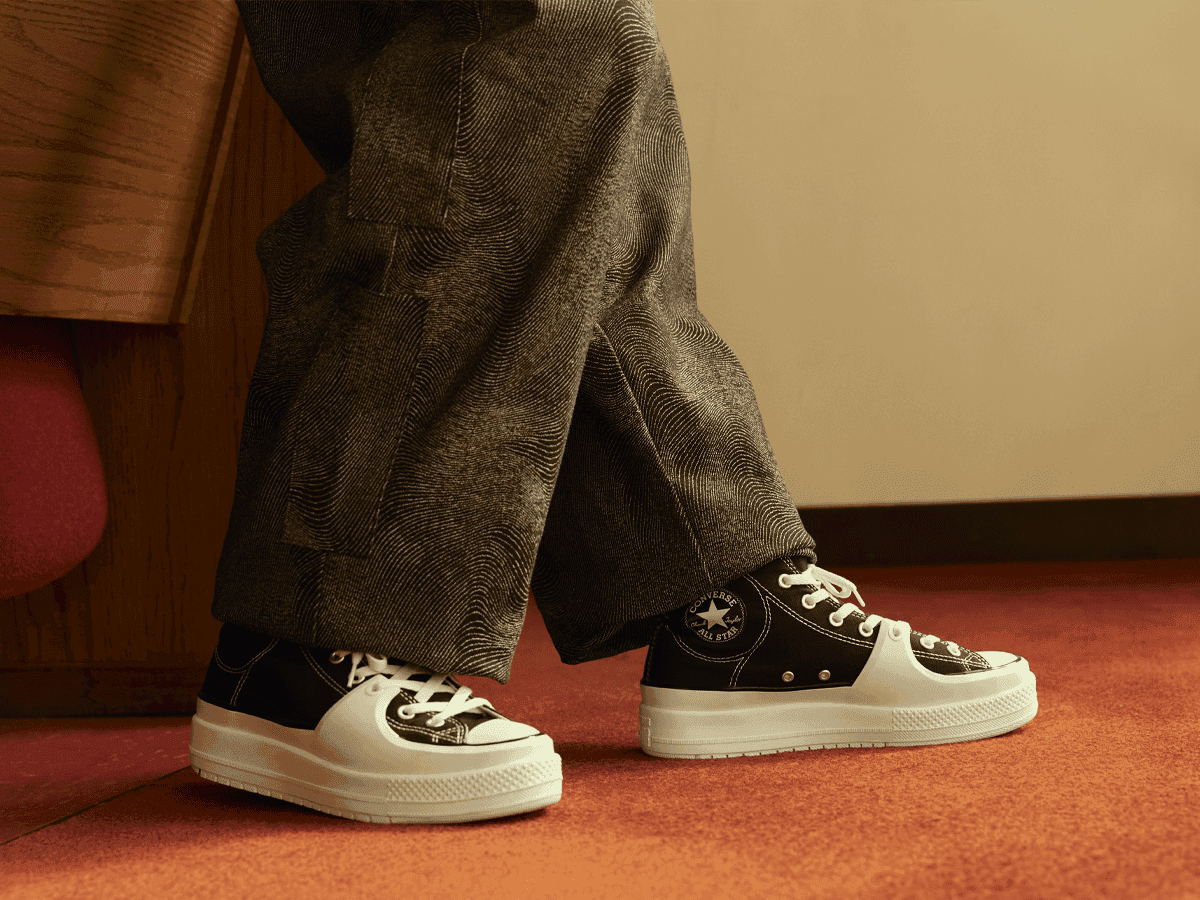 Converse Chuck Taylor All Star Construct sneakers in black and white worn with grey textured trousers on red carpet.
