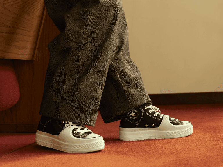 Converse Chuck Taylor All Star Construct sneakers in black and white worn with grey textured trousers on red carpet.