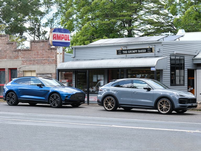 Aston Martin DBX707 and Porsche Cayenne Turbo GT parked outside The Grumpy Baker with lush trees in the background.