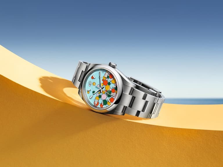 Rolex Oyster Perpetual watch with colourful dial on yellow surface against blue sky background.