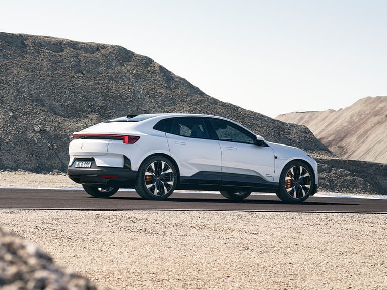 2025 Polestar 4 in white viewed from rear three-quarter angle, parked on a desert road with rocky hills in the background.