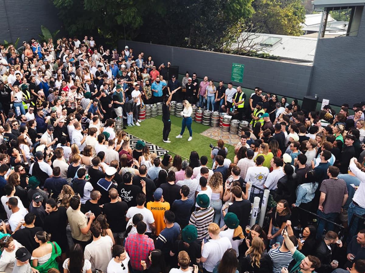 Crowd gathered at The Sackville Hotel courtyard for Two-Up game, with kegs and trees in the background.