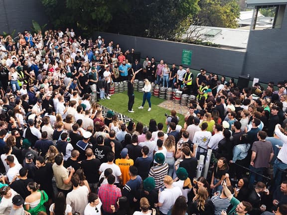 Crowd gathered at The Sackville Hotel courtyard for Two-Up game, with kegs and trees in the background.