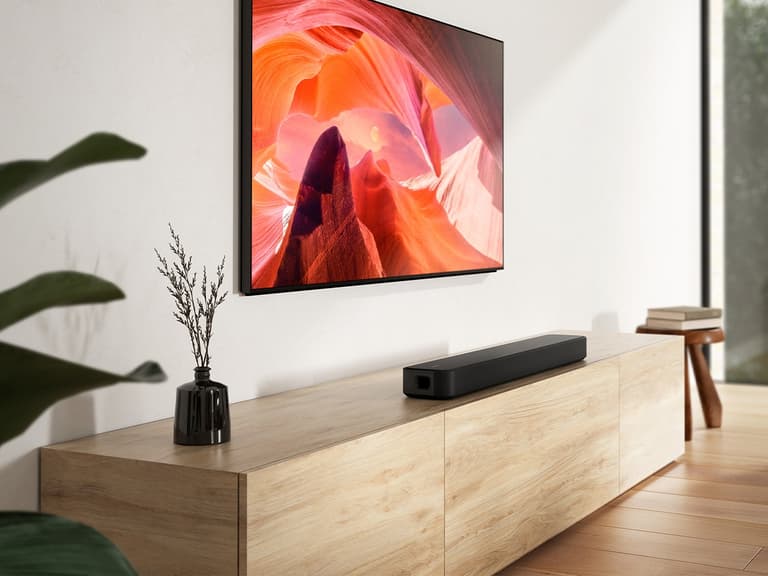 Sony HT-S2000 soundbar on wooden cabinet beneath wall-mounted TV displaying vibrant abstract art.
