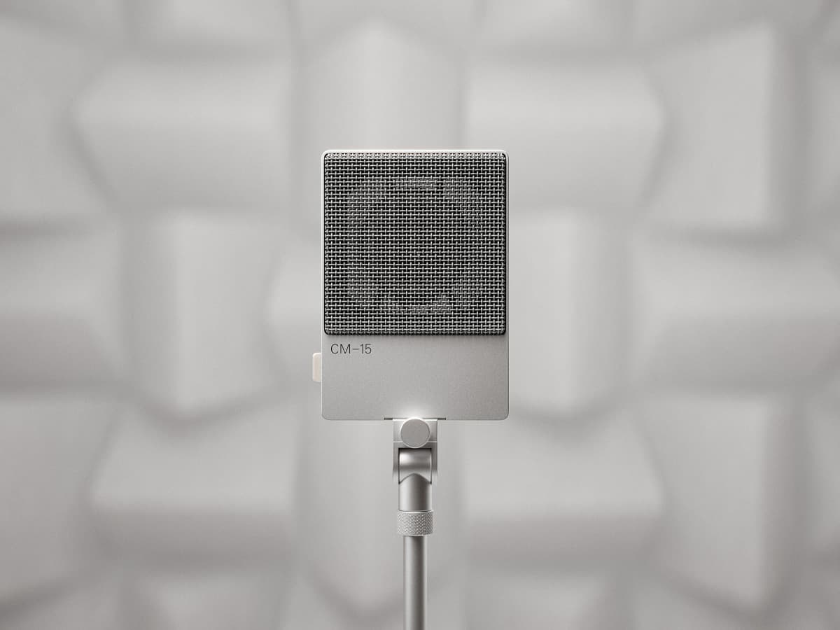 Teenage Engineering CM-15 studio mic in silver with a square grille, set against a geometric acoustic panel backdrop.
