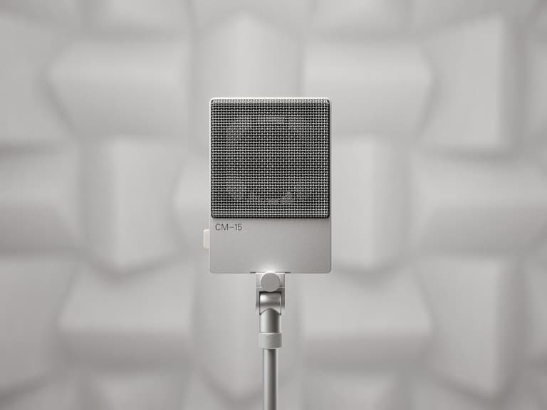 Teenage Engineering CM-15 studio mic in silver with a square grille, set against a geometric acoustic panel backdrop.