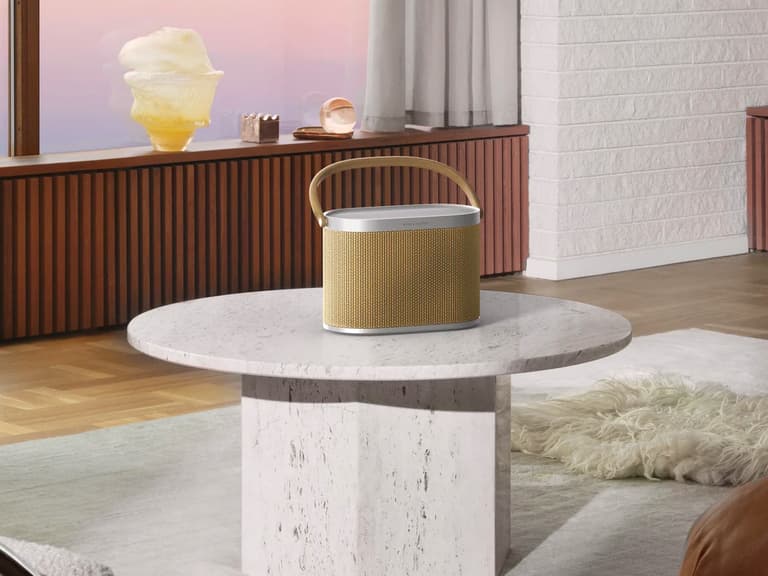 Bang & Olufsen Beosound A5 speaker with a woven texture and leather handle on a marble table in a stylish living room.