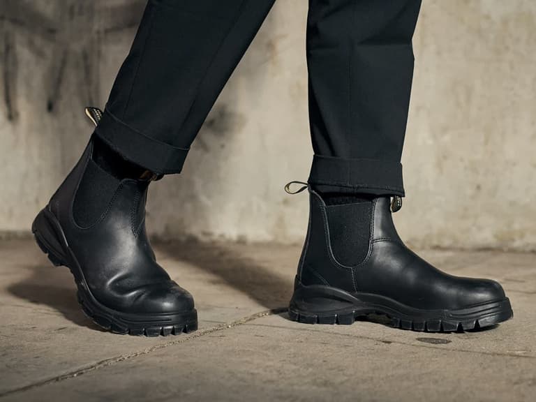 Black leather boots on concrete floor, worn with black trousers, highlighting rugged design.