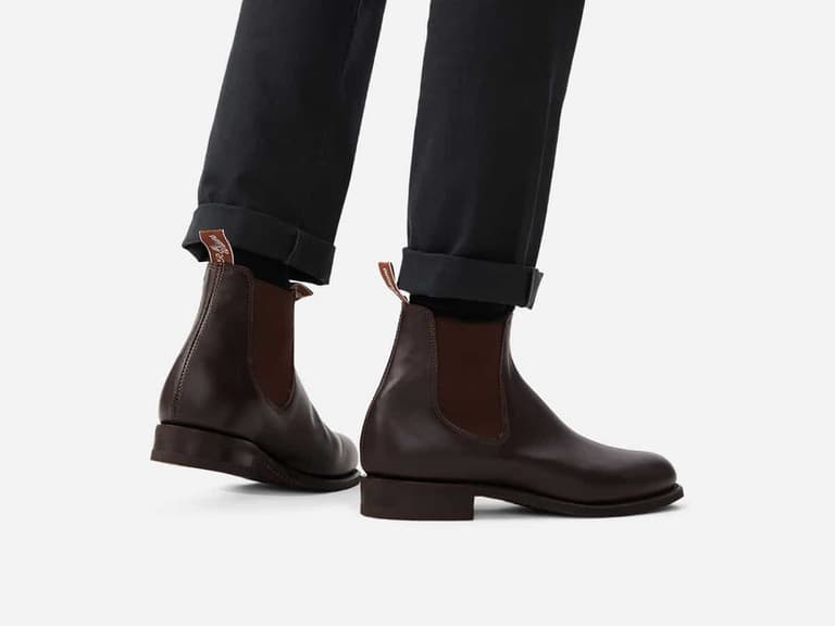 Brown leather Chelsea boots on person wearing black trousers, showing side profile and elastic panels.