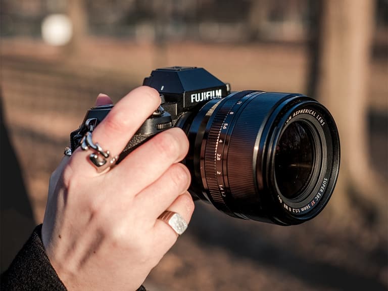 Fujifilm X-S20 camera held outdoors, showing lens detail and hand grip in warm lighting.