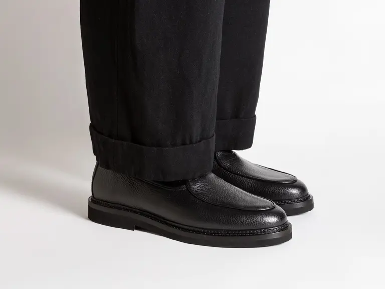 Jacques Soloviere Lex loafers in black leather paired with black trousers.