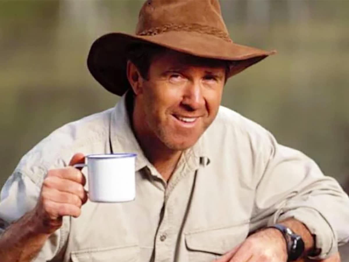 Man in a brown hat holding a white enamel mug outdoors.