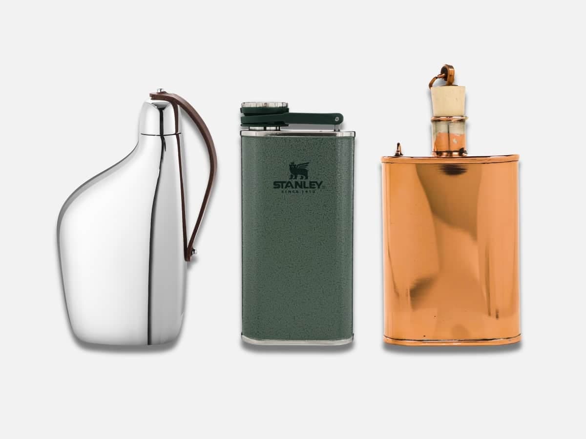 Three hip flasks including a polished silver, a green Stanley, and a copper flask on a white background.