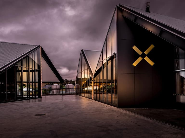 Modern distillery buildings with angular roofs and large glass windows under a dramatic cloudy sky.