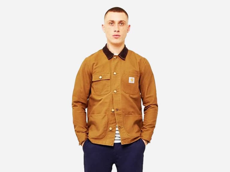 Man wearing a brown Carhartt chore coat with black collar, hands in pockets, against a white background.