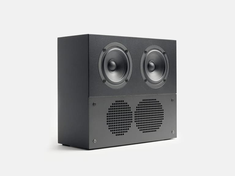 Nocs Design Mini speaker in black with dual drivers and a perforated grille, set against a white background.