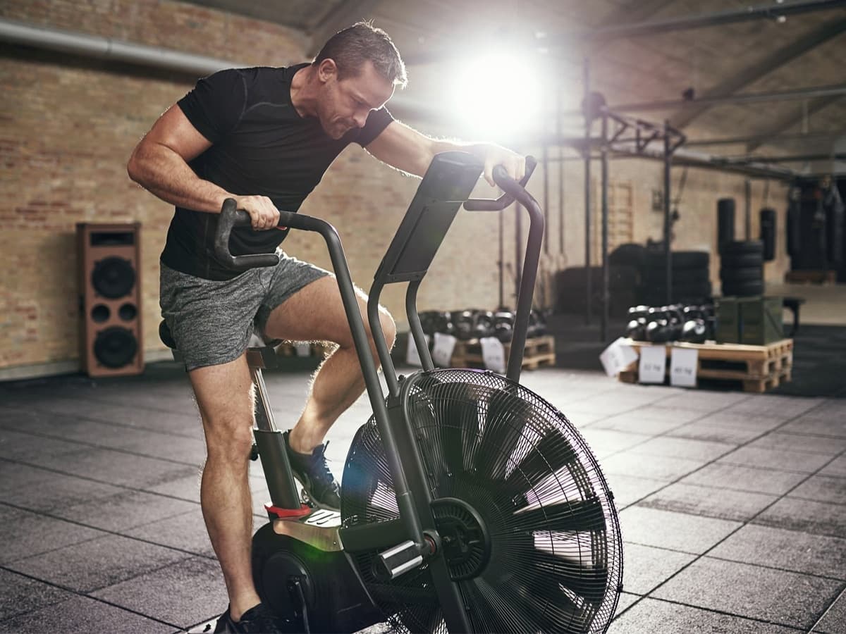 Man in sportswear sitting on cycling machine and riding fast in modern gym