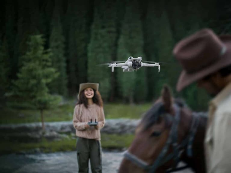 DJI Mini 4 Pro drone flying in a forest with a woman controlling it and a man on horseback nearby.